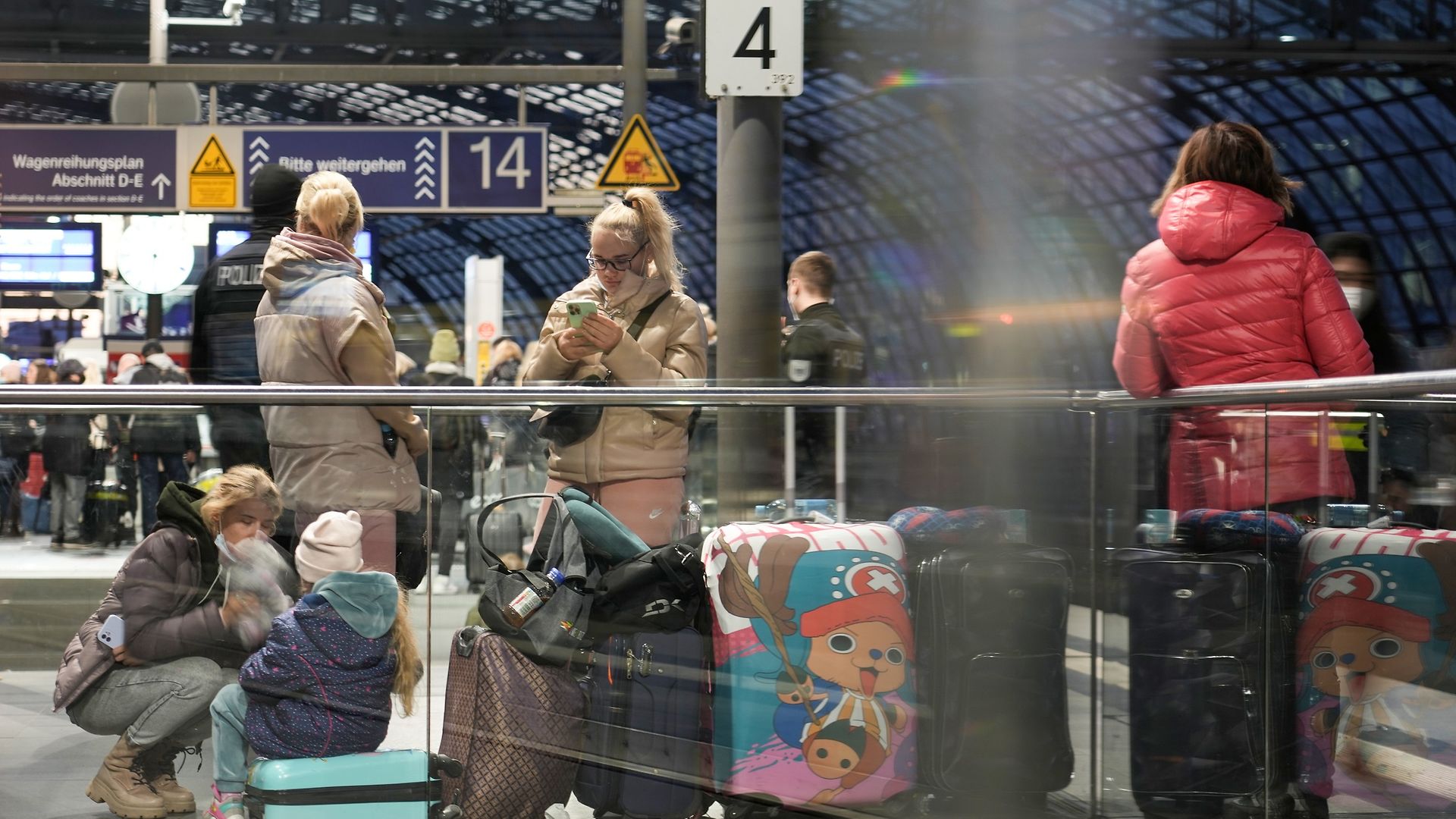 Ukrainische Geflüchtete warten am Bahnsteig. Ein Kind sitzt auf einem Koffer, eine Frau schaut auf ihr Handy.