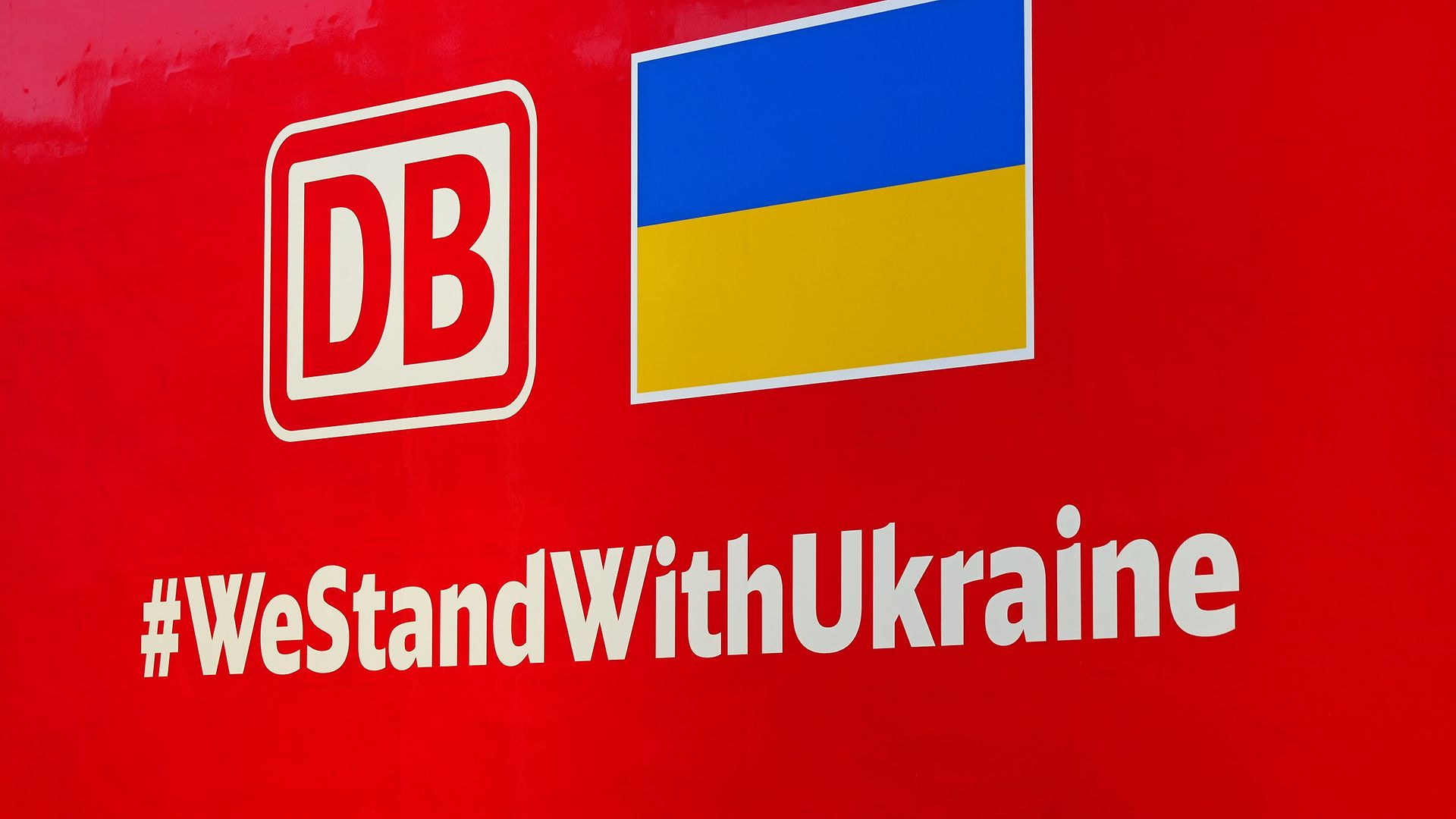 Schriftzug #WeStandWithUkraine und Flaggen der Ukraine und der DB auf roter DB Cargo Lok