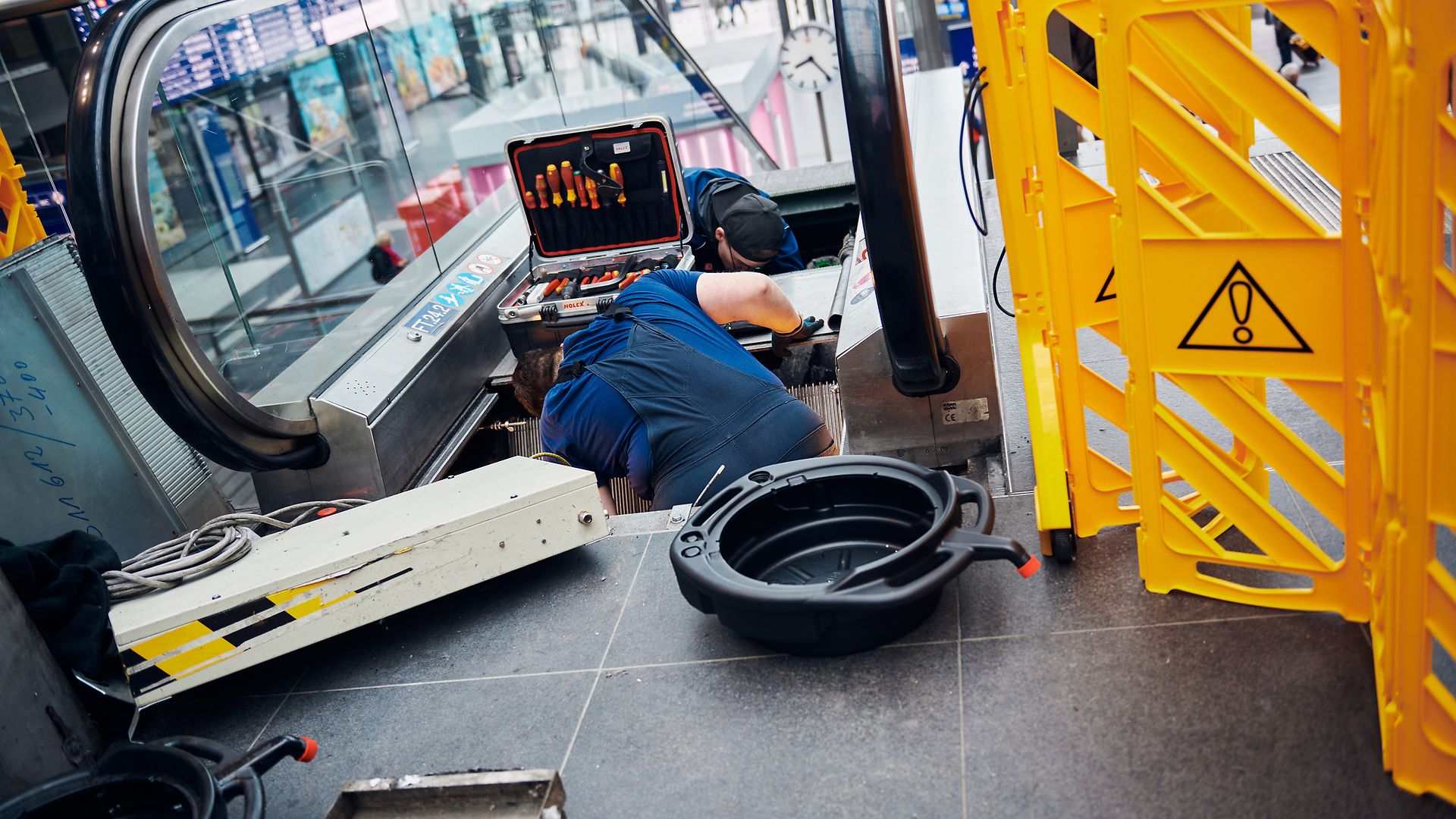 Zwei Techniker reparieren eine Rolltreppe.