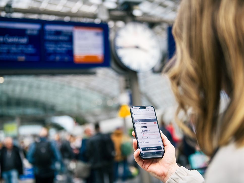 Eine Kundin schaut am Bahnsteig auf Ihr Handy in den DB Navigator